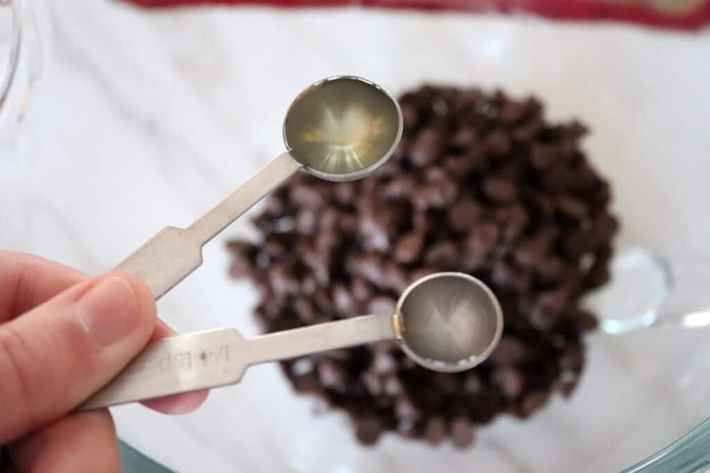 vegetable oil and mint extract in measuring spoons over a bowl of chocolate chips