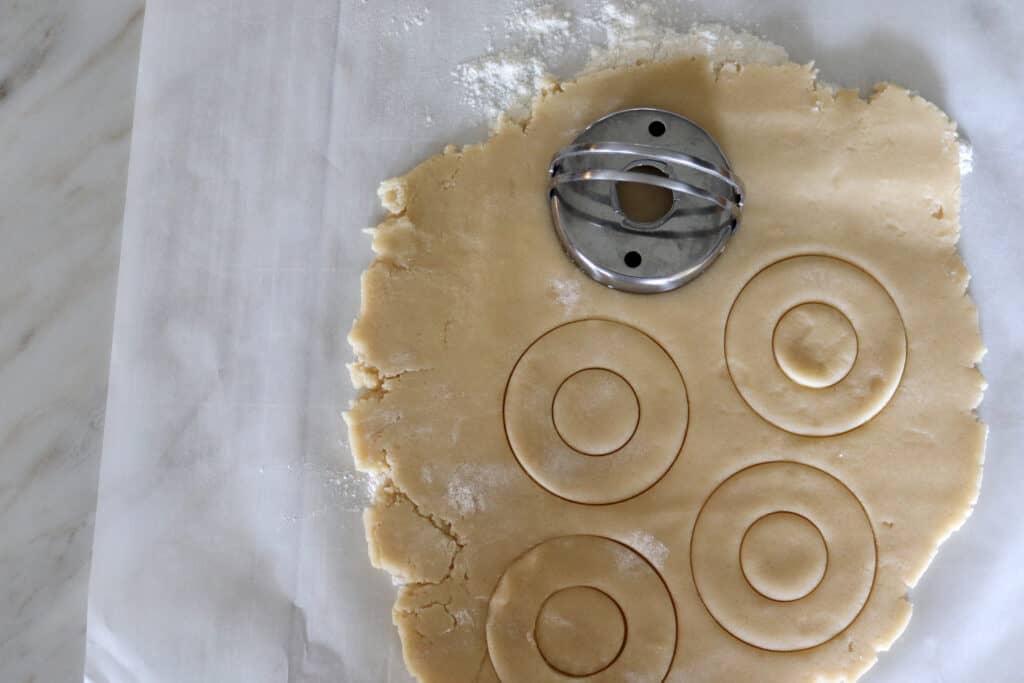 a donut cookie cutter that has cut some shapes into the cookie dough on a flour surface