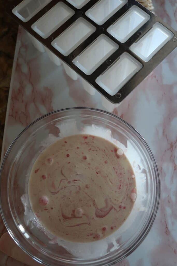 raspberry creamsicle mixture in a bowl with popsicle molds nearby