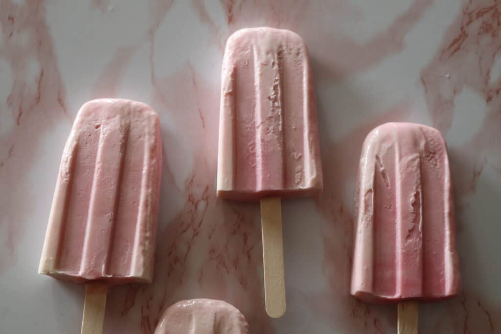 three raspberry creamsicles laying on a pink marble slab