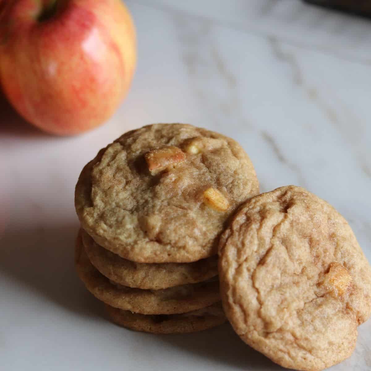 homemade apple snickerdoodle cookies stacked next to apples